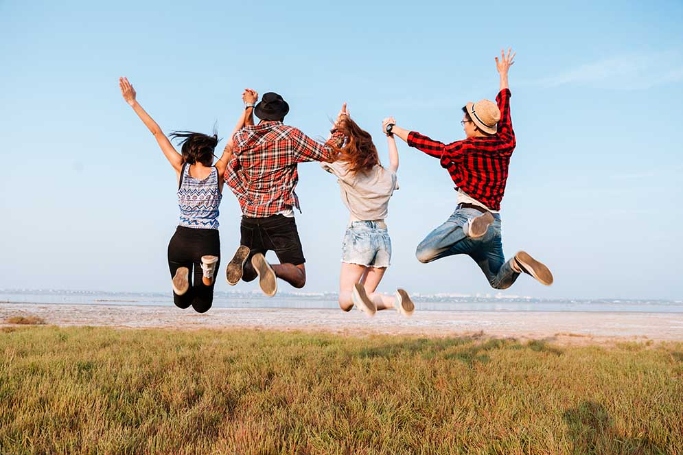 Back view of happy excited young people holding hands and jumping in the air outdoors