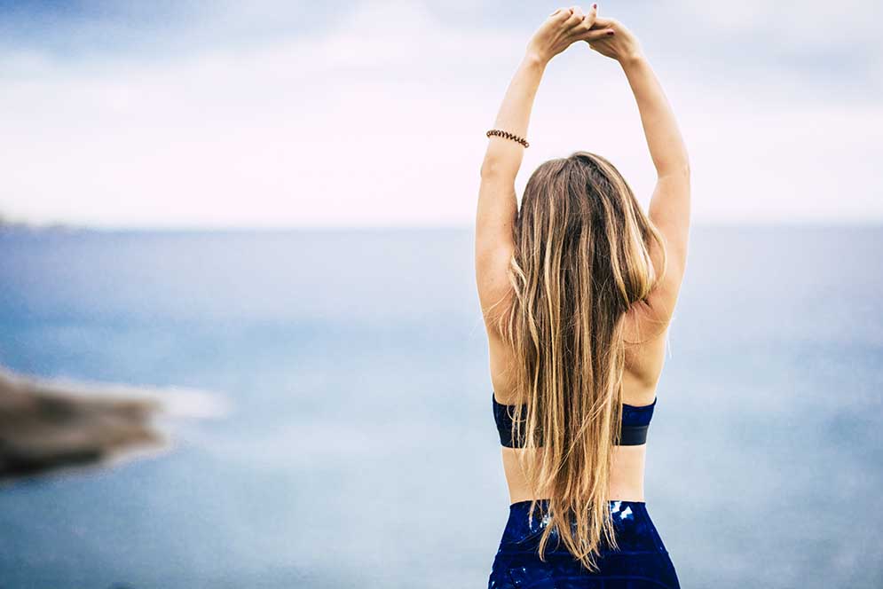 Healthy lifestyle people concept with beautiful long blonde hair girl viewed from back do some stretching in front of the ocean view outdoor - fit woman and attractive female